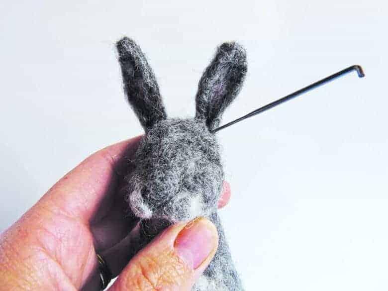 An image of a hand holding a needle felting needle and woolen rabbit.